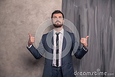 Good looking handsome businessman is standing in his office pointing fingers to the sides and looking up. wearing suit and a tie Stock Photo