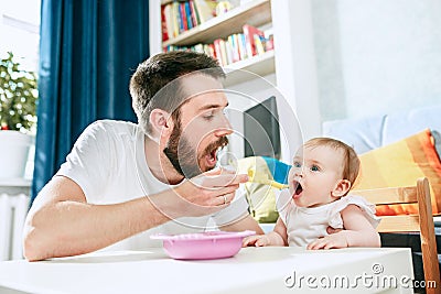 Good looking young man eating breakfast and feeding her baby girl at home Stock Photo