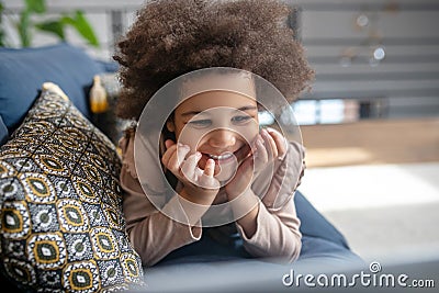 Cute joyful little girl lying on couch on stomach Stock Photo