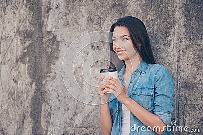 Good morning! Cheerful pretty young serene brunette lady is having hot tea near concrete wall outside, smiling, wearing cozy casua Stock Photo