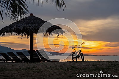 Good morning concept. Nature landscape background. Silhouette bicycle orange dawn mountain sea tropical beach sunbeds Stock Photo