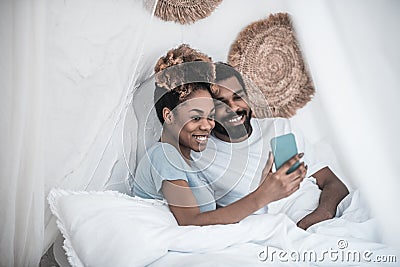 Darkskinned woman and man taking selfie in bed Stock Photo
