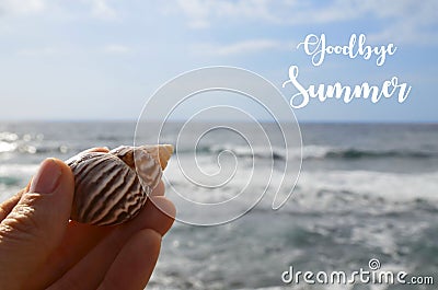 Goodbye Summer greeting card with hand holding sea shell on a blue ocean water background. Stock Photo