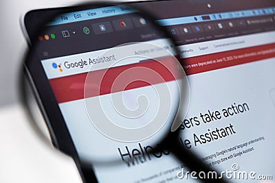 Google Assistant logo enlarged through a magnifying glass on a laptop screen Editorial Stock Photo