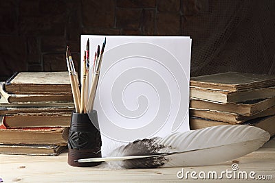 Goose feather and a glass with dirty brushes on the background of old books and sheets of white paper. Retro stylized photo Stock Photo