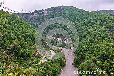 A gorge in the mountains with a suspension bridge over it. Skybridge suspension bridge over a precipice on a cloudy day. SkyPark, Stock Photo