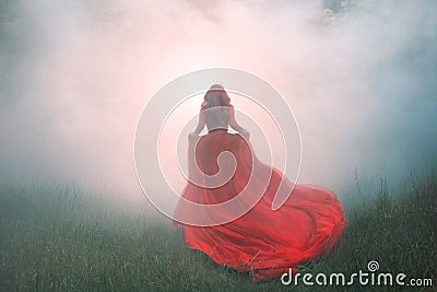 Gorgeous amazing wonderful scarlet red dress with a long flying waving train, a mysterious girl with red curly hair runs Stock Photo