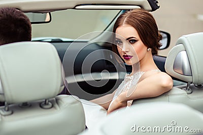 Gorgeous bride with fashion makeup and hairstyle in a luxury wedding dress with handsome groom near white cabriolet car Stock Photo