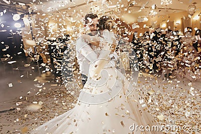 Gorgeous bride and stylish groom dancing under golden confetti a Stock Photo