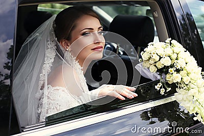 Gorgeous bride in wedding dress with bouquet of flowers posing in car Stock Photo