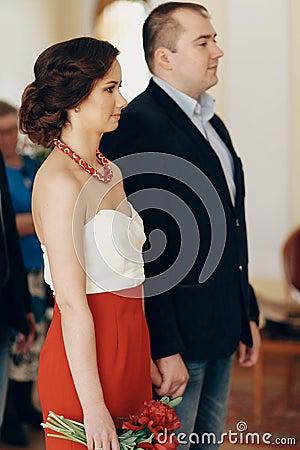 Gorgeous brunette bride holding hands with smiling groom at wedding registry office, cute stylish couple before wedding ceremony Stock Photo