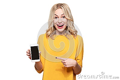 Gorgeous excited woman pointing to blank screen on mobile phone over white background, celebrating victory and success. Excitement Stock Photo