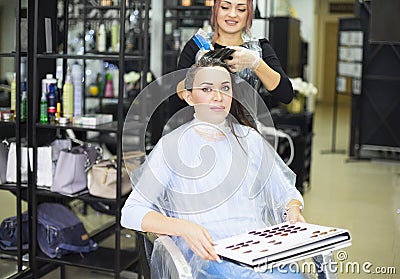 Gorgeous happy woman looking to the camera while examining hair dye color chart with her hairdresser at the beauty salon treatment Stock Photo