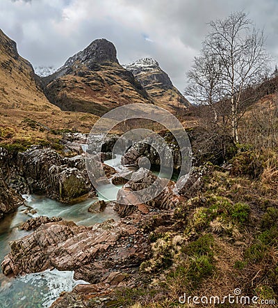 Gorgeous landscape image of vibrant River Coe flowing beneath snowcapped mountains in Scottish Highlands Stock Photo