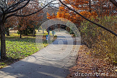 A gorgeous shot of a long smooth winding footpath in the park surrounded by gorgeous autumn colored trees with blue sky and clouds Editorial Stock Photo