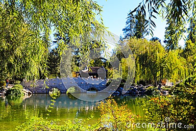 A gorgeous shot of the stone bridge with 3 circles over the green lake surrounded by lush green and autumn colored trees Stock Photo