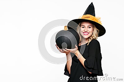 Gorgeous smiling Halloween Witch holding large black pumpkin. Portrait of a beautiful young woman wearing witch hat. Halloween. Stock Photo