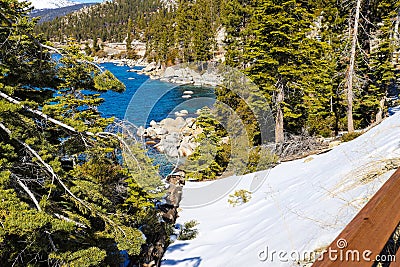 A gorgeous smooth concrete paved hiking trail with a burnt orange wooden fence along the trail with lush green pine trees and snow Stock Photo