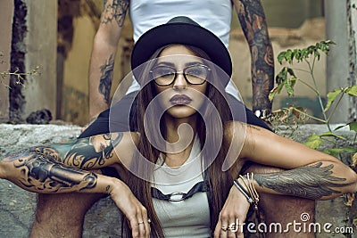 Gorgeous tattooed girl with provocative make up sitting between her boyfriend's legs in the ruined abandoned building Stock Photo