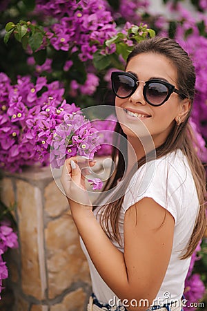 Gorgeous woman in sunglasses stand in beautiful flowers. Portrait of happy smiled young woman Stock Photo