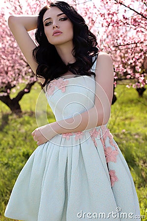 gorgeous young woman in elegant dress posing in garden with blossom peach trees Stock Photo