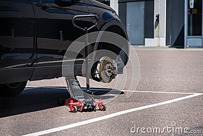 Car lift holding up a black car missing a front wheel on a parking lot.. Editorial Stock Photo