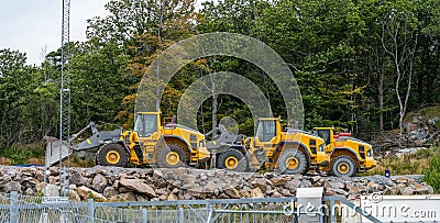 Three yellow Volvo wheel loaders parked by a forest.. Editorial Stock Photo