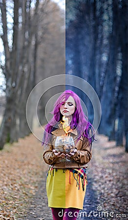 Gothic Girl with purple hair is standing with a burning glass in her hands in the alley in the autumn forest. Concept editing, pho Stock Photo