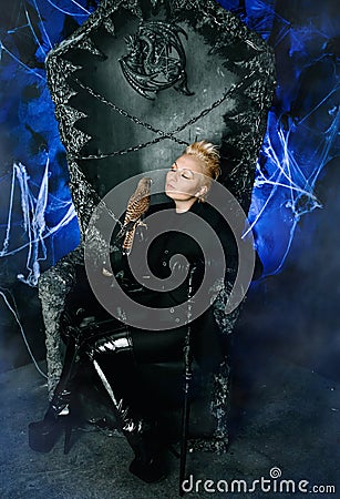 Gothic woman with bird on huge scary throne with blue spooky light ready for Halloween party Stock Photo