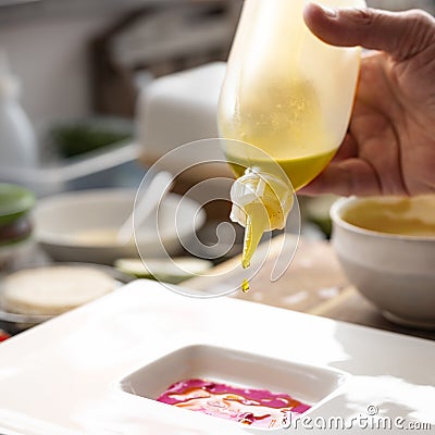 Gourmet chef dripping precious oil from a bottle into a beetroot sauce to prepare a menu course on a white plate, creative cooking Stock Photo