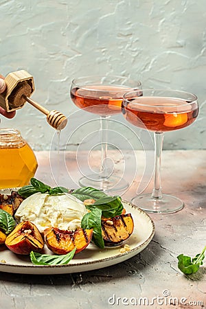 Gourmet Roasted Peaches with Burrata soft cheese, basil and drizzled with honey, with rose wine. Antipasto Dinner or aperitivo Stock Photo