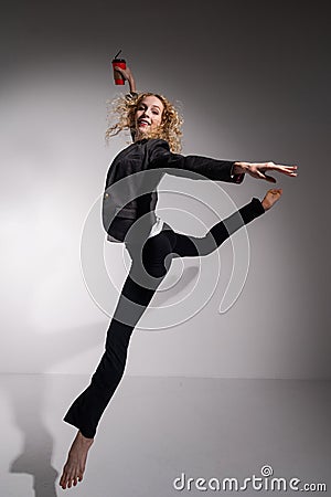 Graceful barefoot ballerina in a business suit jumping with a glass of coffee in her hands on a white background. Stock Photo