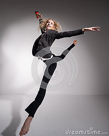 Graceful barefoot ballerina in a business suit jumping with a glass of coffee in her hands on a white background. Stock Photo