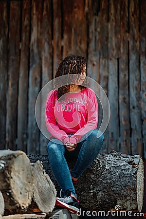 Graceful curly-haired woman having fun during photoshoot. Lovely tanned girl in pink shirt posing on wooden background. Stock Photo