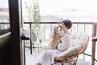 Graceful dark-haired woman in bathrobe kissing beagle dog and looking away thinking about something. Portrait of lady Stock Photo