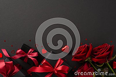 Overhead shot featuring chocolate candy, gift boxes with elegant bows, red roses, confetti on refined black background Stock Photo