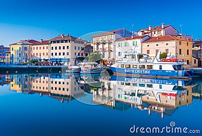 Grado, Italy: Colored residential buildings and boats are mirror reflected in sea water Editorial Stock Photo