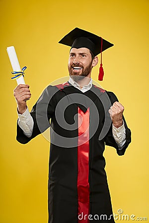 Graduate with beard holding diploma, showing hurray. Stock Photo
