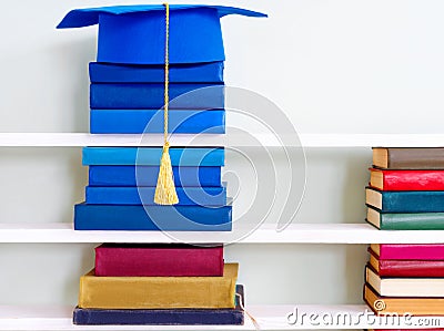 Graduation blue mortarboard on top of stack of books on wooden shelf Stock Photo