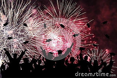 Graduation ceremony, fireworks in night sky. Silhouette of happy graduate students throwing academic square caps Stock Photo