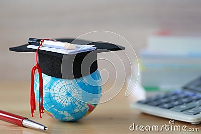 Graduation hat on blue globe with stack of coins money on wooden background, Saving money for education concept Stock Photo