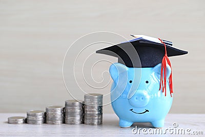 Graduation hat on blue piggy bank with stack of coins money on wooden background, Saving money for education concept Stock Photo