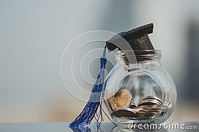 Graduation hat on coins money in the glass bottle on white background. Stock Photo