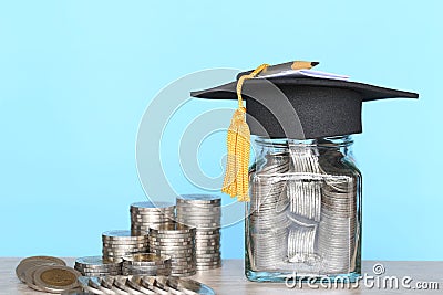 Graduation hat on the glass bottle with Stack of coins money on blue background, Saving money for education concept Stock Photo