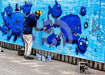 Graffiti painter paiting a wall with blue fish cartoon pictures of several fishes in Taolin in Estonia. Eastern European artist. Editorial Stock Photo