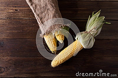 Grains of ripe corn on wooden background. Corn cob and green leaves on wooden background, Stock Photo