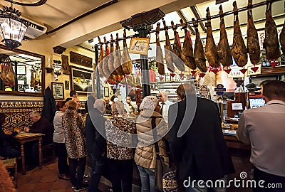 People drinking and eating at traditional tapas bar with dry-cured ham legs and vintage decor Editorial Stock Photo