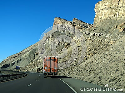 Orange semi truck drives past cliffs Editorial Stock Photo