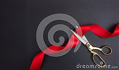 Grand opening. Top view of gold scissors cutting red silk ribbon against black background Stock Photo