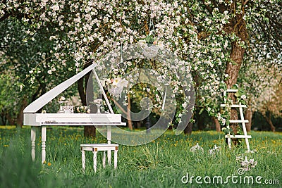 Grand piano and white staircase with romantic decor in spring in a blossoming Apple tree garden Stock Photo